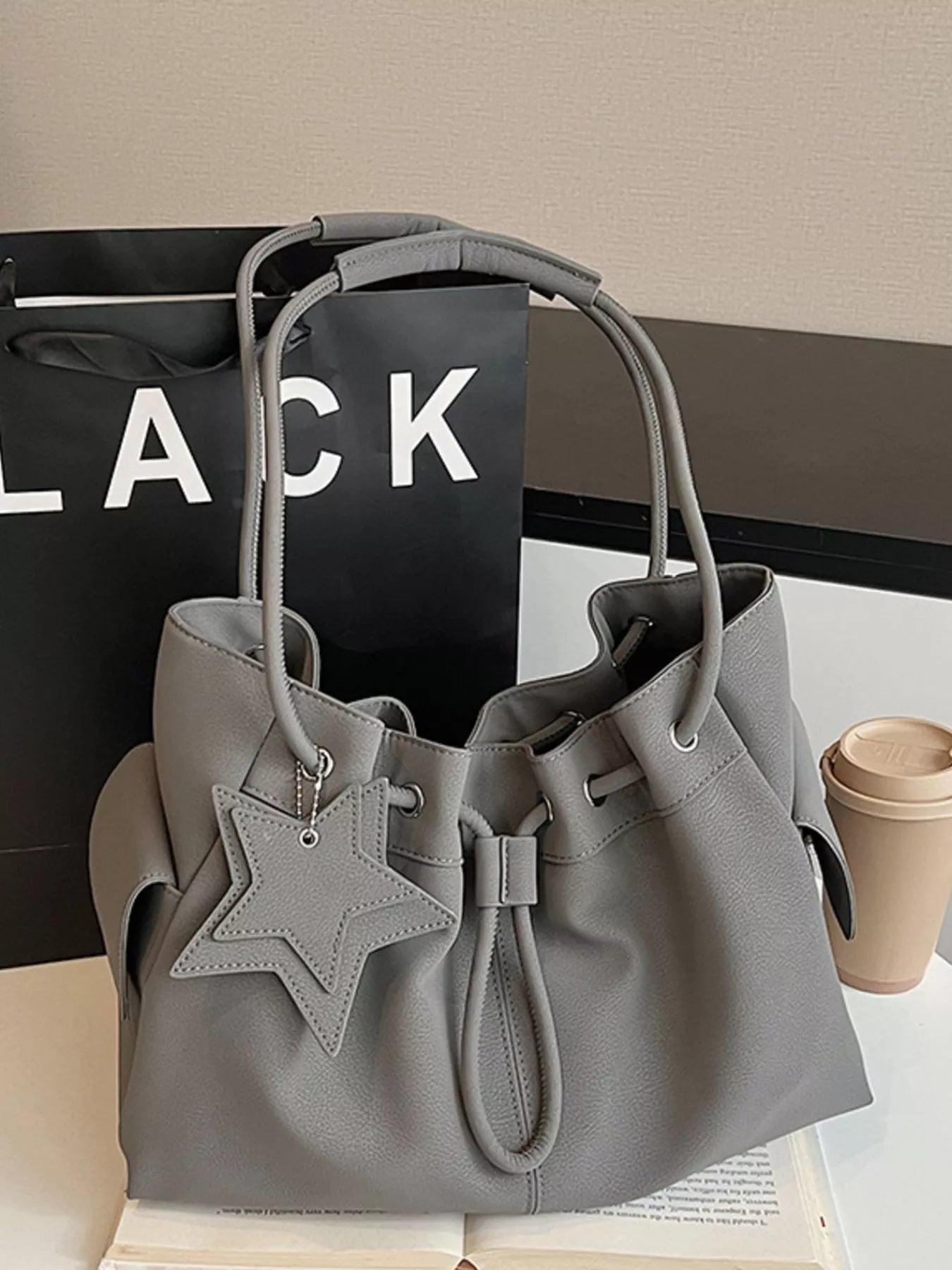 Drawstring shoulder bag with star charm, trendy handbag by Trendsi featuring a stylish design and adjustable strap.